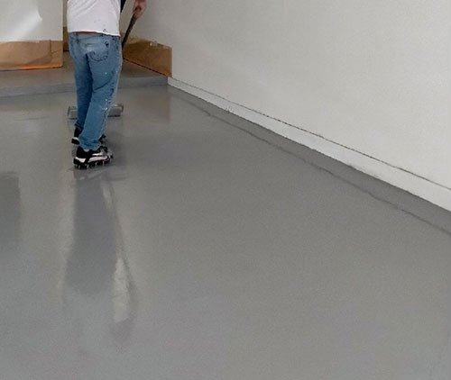 Worker applying a base coat to a concrete floor coating project.